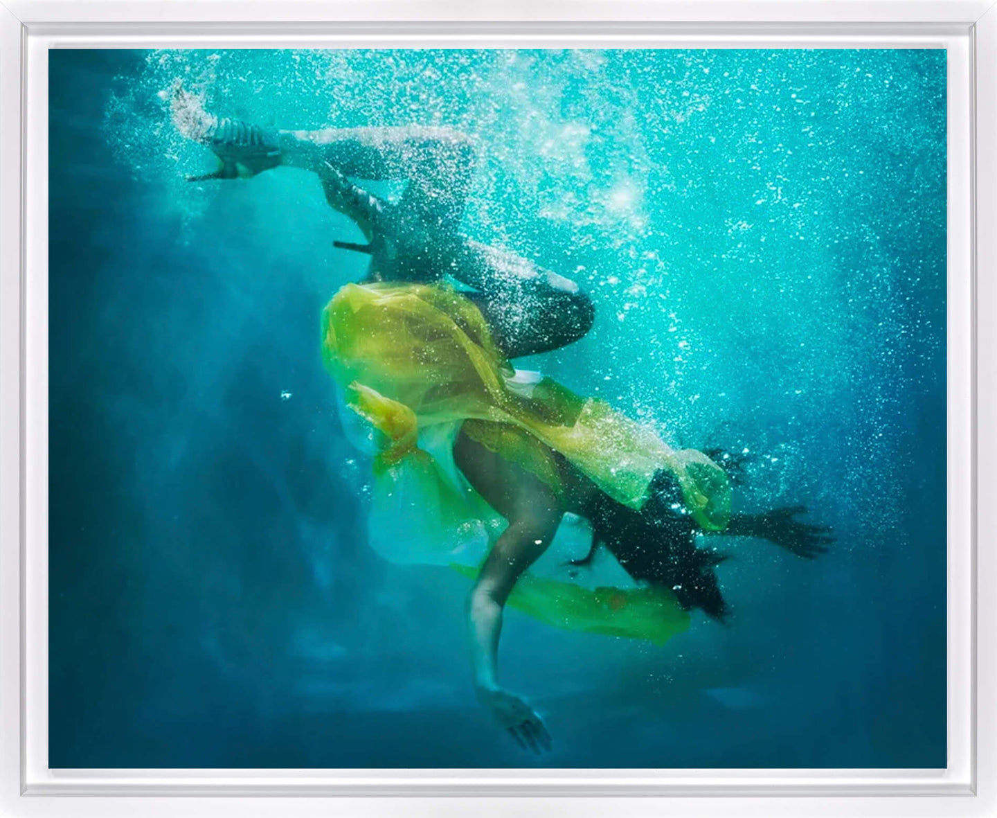 Underwater art print featuring a swimmer in a bright yellow swimsuit swimming through turquoise blue water with rising bubbles, presented in a white frame.