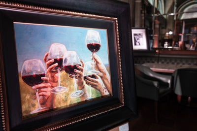 Fabian Perez Framed artwork of hands holding wine glasses in a bar setting