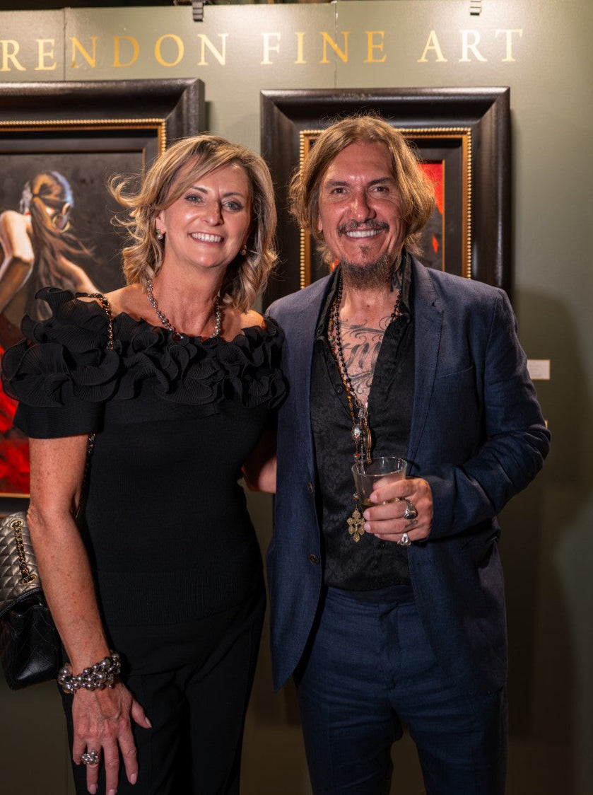 Fabian Perez posing in front of a 'Fine Art' display with artworks in the background.